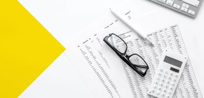 Glasses, calculator, and pencil on top of personal finance documents near a keyboard
