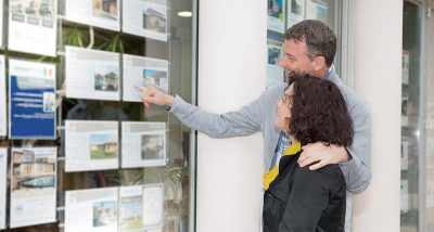 Couple looking at photos of properties in the window of a realtor's office